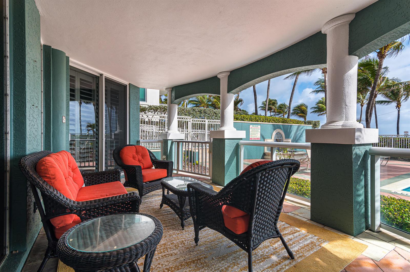 A covered patio features wicker furniture with orange cushions and a view of a pool — 2051 SE 3rd Street # 101, Deerfield Beach FL 33441, DEERFIELD BEACH, FL