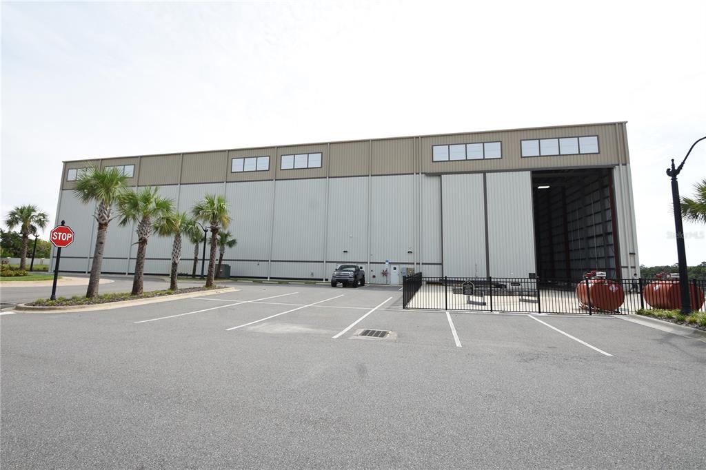 A large metal warehouse building features a parking lot, palm trees, and a stop sign — 114 DEL PALMA DRIVE, PALM COAST, FL
