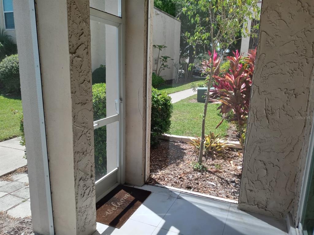 A view from a tiled patio through a screen door toward a landscaped outdoor area — 536 ORANGE DRIVE UNIT 14, ALTAMONTE SPRINGS, FL
