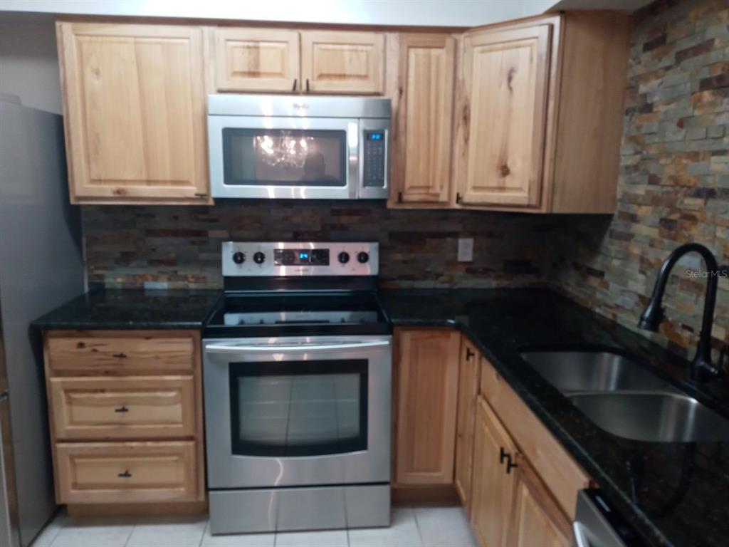 A kitchen with wood cabinets, stainless steel appliances, dark countertops, and a stone tile backsplash — 536 ORANGE DRIVE UNIT 14, ALTAMONTE SPRINGS, FL