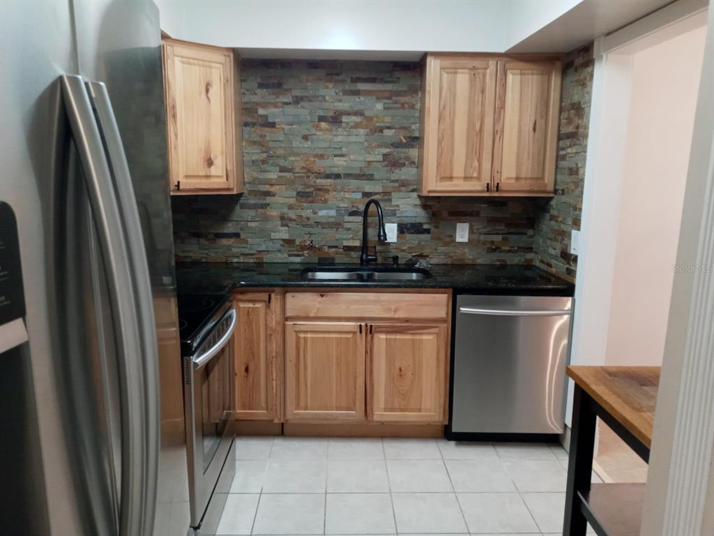 A kitchen features wood cabinets, dark countertops, a stone tile backsplash, and stainless steel appliances — 536 ORANGE DRIVE UNIT 14, ALTAMONTE SPRINGS, FL