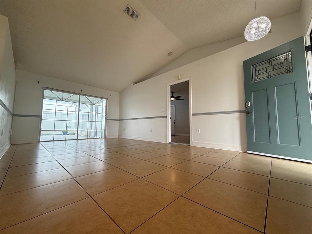 An empty room with tan tile flooring, a vaulted ceiling, and a teal front door — 2531 SAGE DRIVE, KISSIMMEE, FL