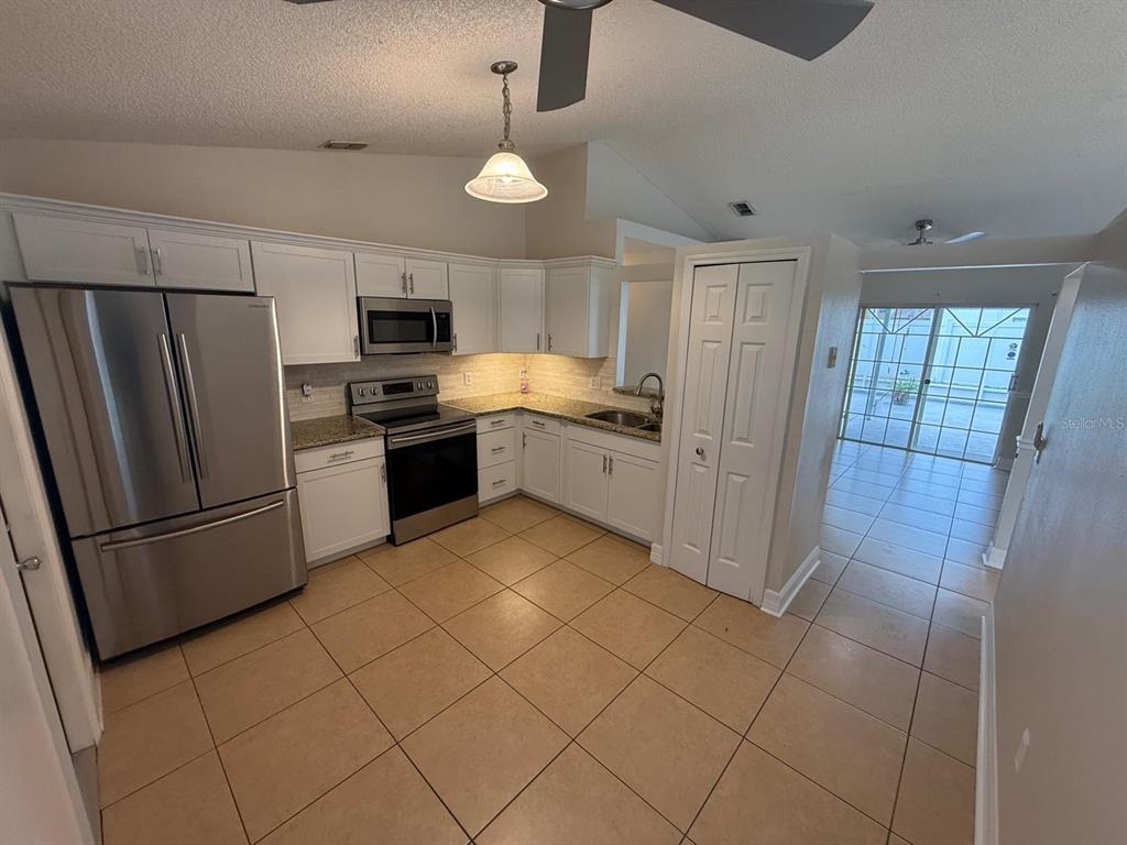 A kitchen with white cabinets, stainless steel appliances, granite countertops, and beige tile flooring — 2531 SAGE DRIVE, KISSIMMEE, FL