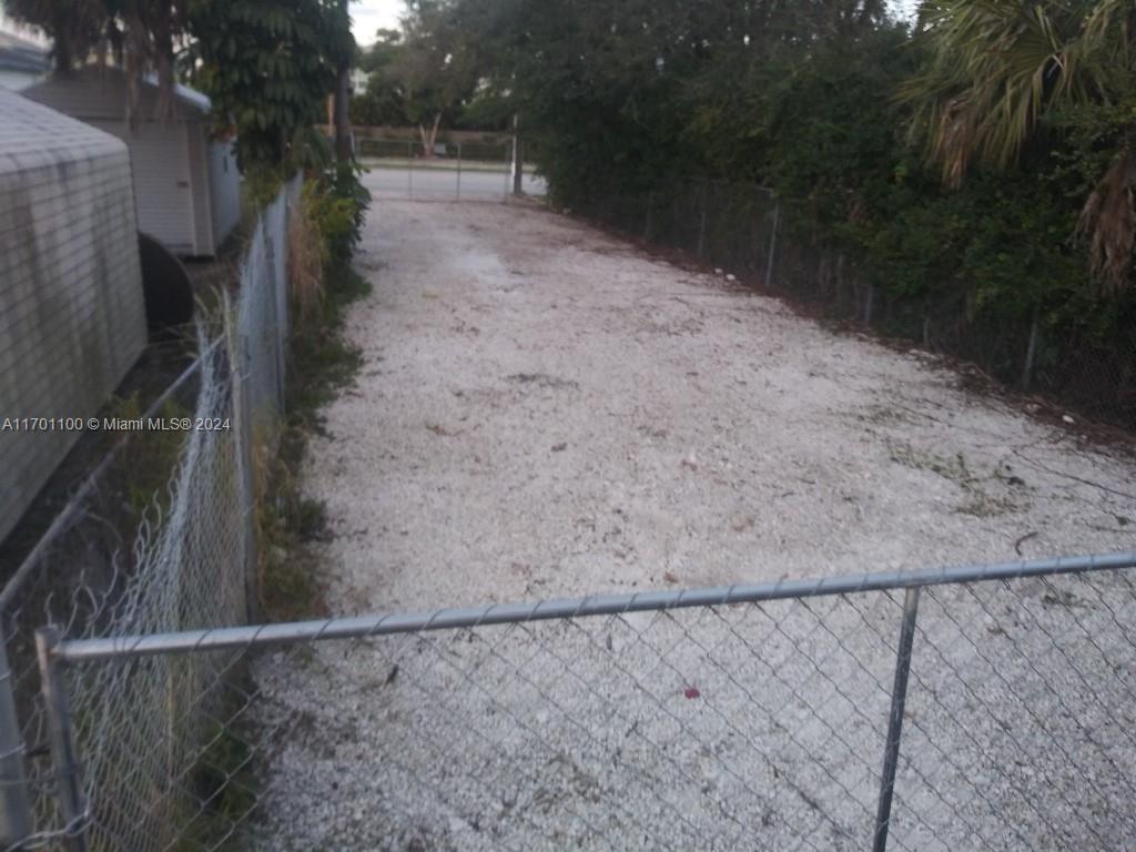 A gravel-covered lot is enclosed by chain-link fencing with trees and bushes in the background — Pembroke Rd, West Park FL 33023, WEST PARK, FL