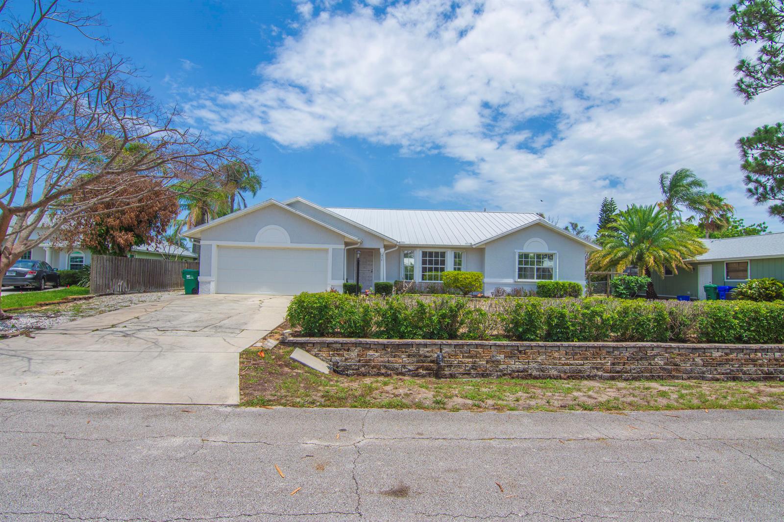A single-story house with a white metal roof, concrete driveway, and a brick retaining wall — 474 Arbor Street, Sebastian FL 32958, SEBASTIAN, FL