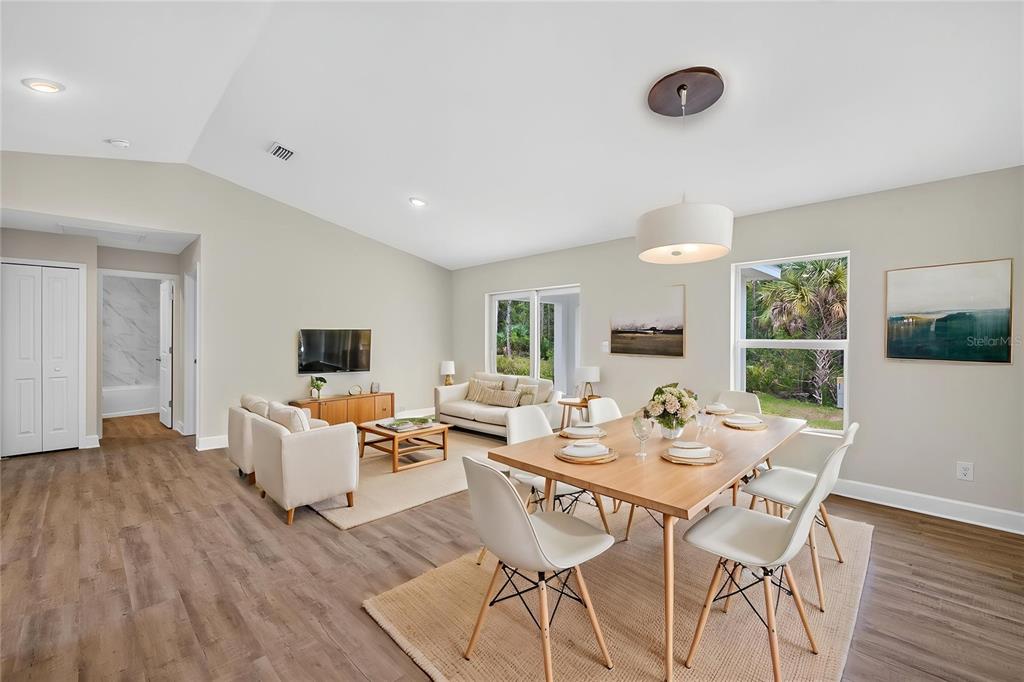 An open-concept living and dining area features light wood flooring, vaulted ceilings, and large windows — 23477 BRANCH AVENUE, PORT CHARLOTTE, FL