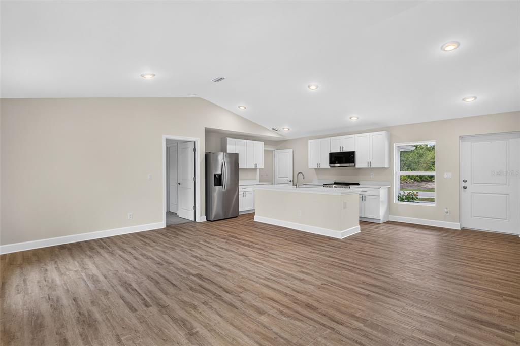 An open-concept kitchen and living area features white cabinetry, stainless appliances, and wood-look flooring — 23477 BRANCH AVENUE, PORT CHARLOTTE, FL