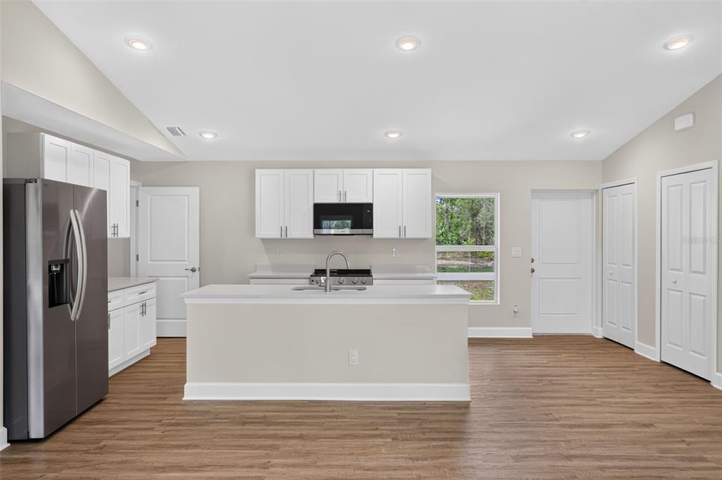 A kitchen with white cabinets, stainless steel appliances, a center island, and wood-look flooring — 23477 BRANCH AVENUE, PORT CHARLOTTE, FL