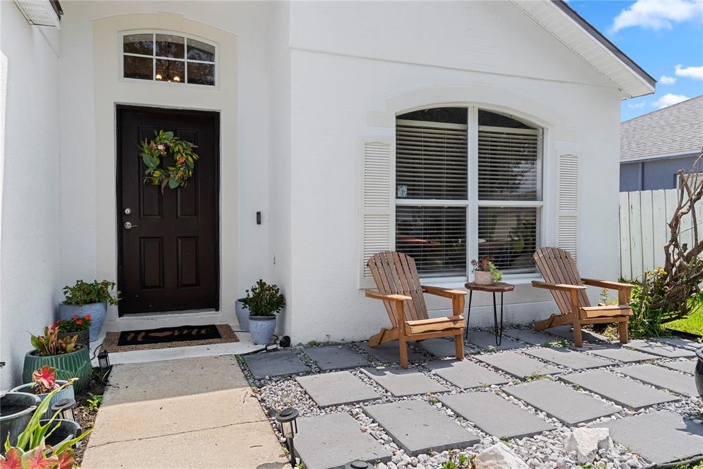 A white house exterior features a dark front door, a stone patio, and two wooden chairs — 234 GRAND ROYAL CIRCLE, WINTER GARDEN, FL