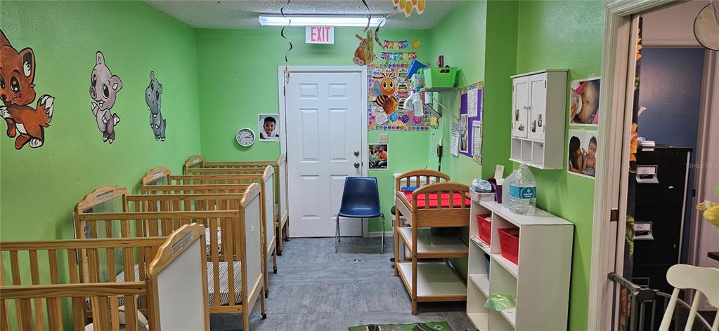 A daycare nursery room features several wooden cribs, a changing table, and lime green walls — 229 AVENUE K SE, WINTER HAVEN, FL
