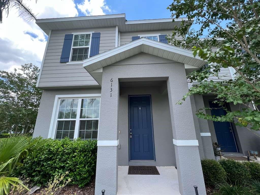 A two-story residential building with gray siding stands at a street corner with landscaping — 6131 ELFIN HERB WAY, WINTER GARDEN, FL