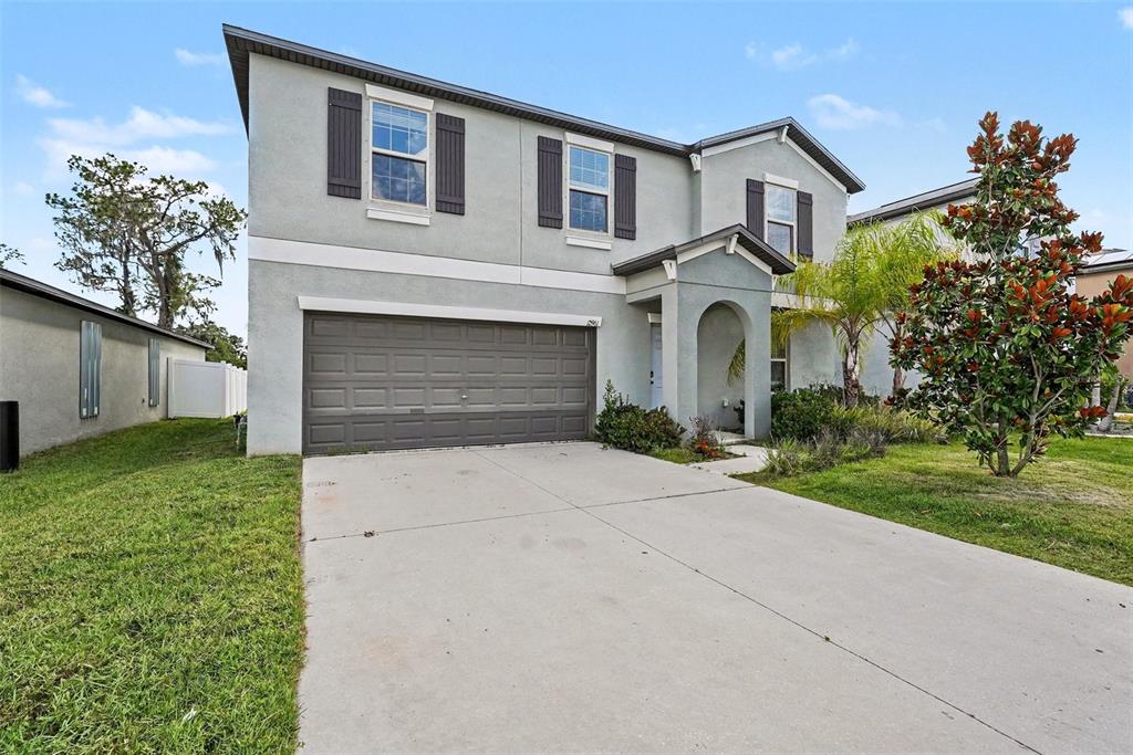 A two-story house with a gray stucco exterior, a two-car garage, and a front porch — 12961 WILDFLOWER MEADOW DR, RIVERVIEW, FL