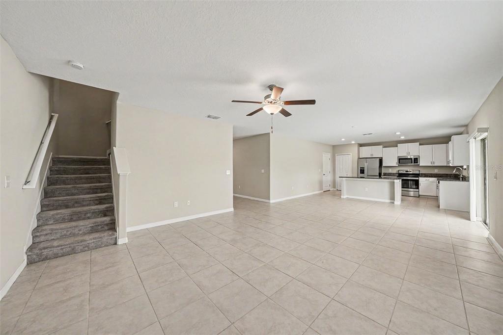 An open-concept living area with tile flooring, a carpeted staircase, and a kitchen with appliances — 12961 WILDFLOWER MEADOW DR, RIVERVIEW, FL