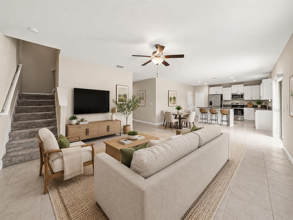 An open-concept living room with a staircase, kitchen, and dining area on tile flooring — 12961 WILDFLOWER MEADOW DR, RIVERVIEW, FL