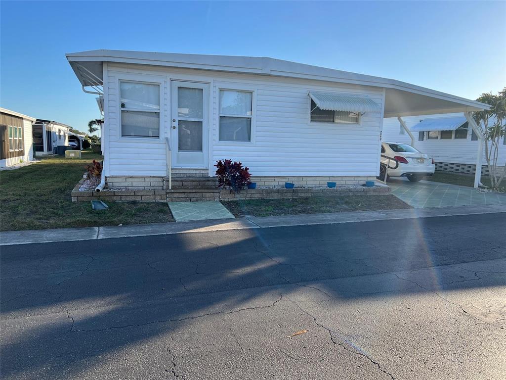 A white mobile home with a carport, front steps, and a brick-style foundation — 220 ROYAL PALM CIRCLE, LARGO, FL