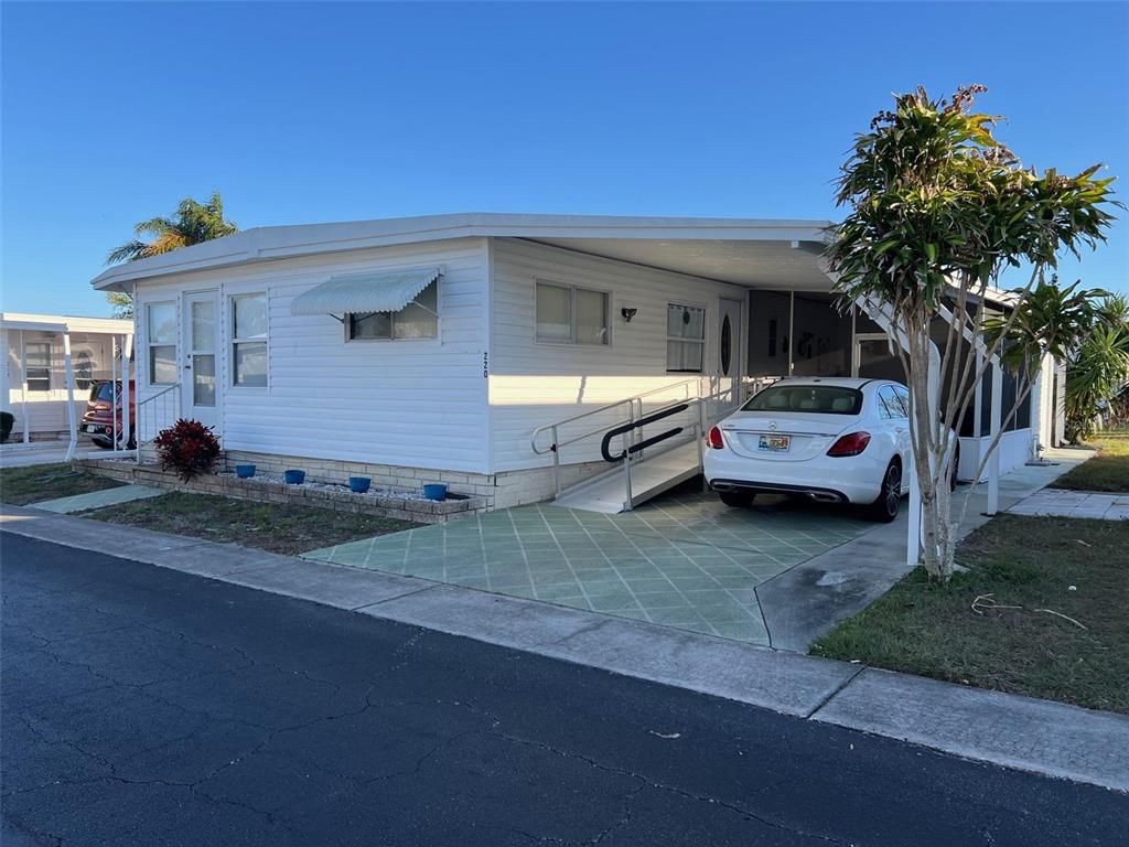 A white mobile home features a carport, a wheelchair ramp, and a small front garden — 220 ROYAL PALM CIRCLE, LARGO, FL