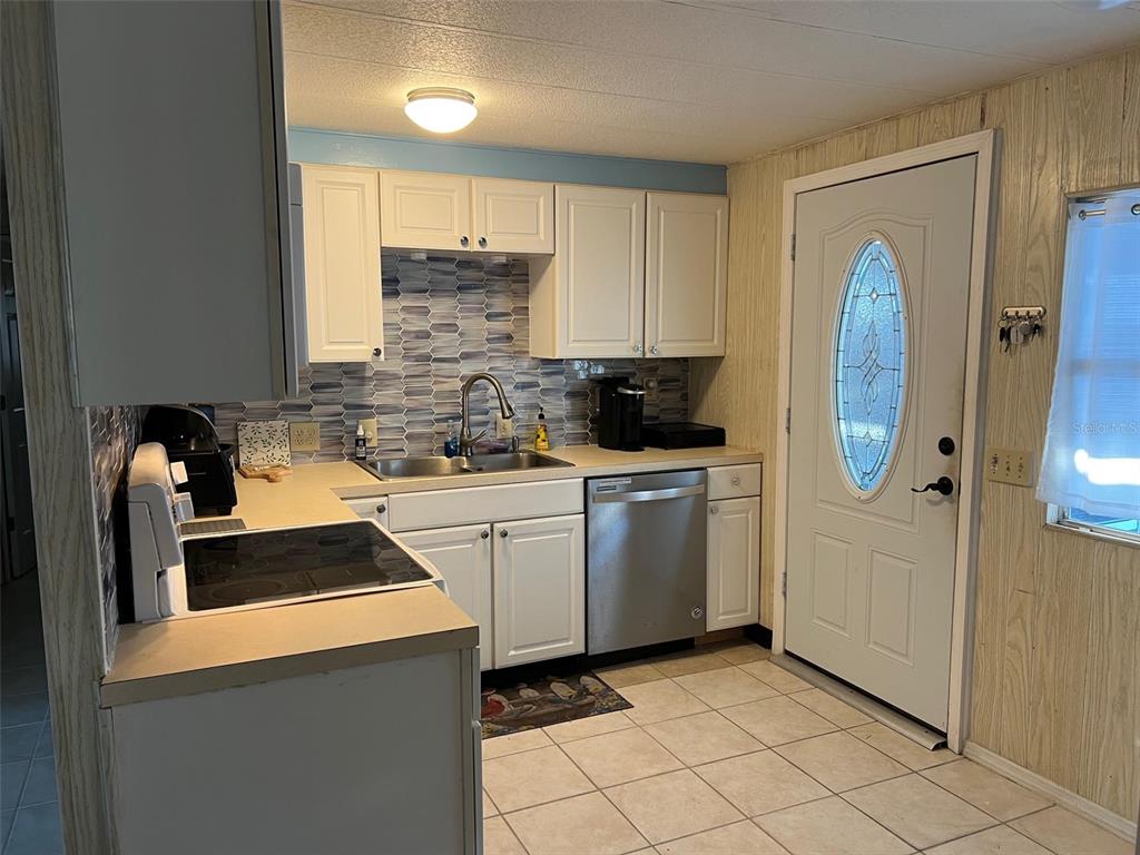 A kitchen features white cabinets, a patterned tile backsplash, stainless steel appliances, and tile flooring — 220 ROYAL PALM CIRCLE, LARGO, FL