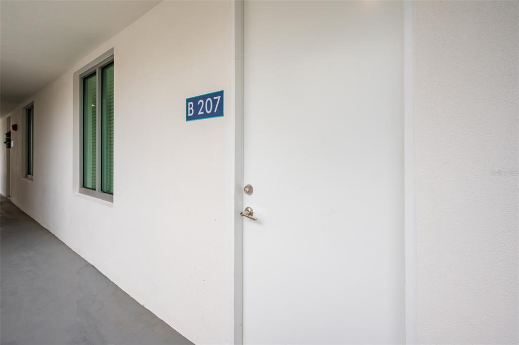A white exterior door labeled B 207 is located in a hallway with gray flooring — 1703 N TAMIAMI TRAIL UNIT 207, SARASOTA, FL