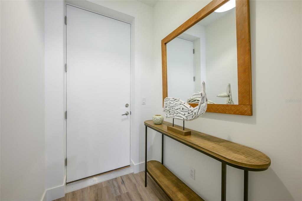 An entryway features a white door, a wooden console table, and a rectangular wall mirror — 1703 N TAMIAMI TRAIL UNIT 207, SARASOTA, FL