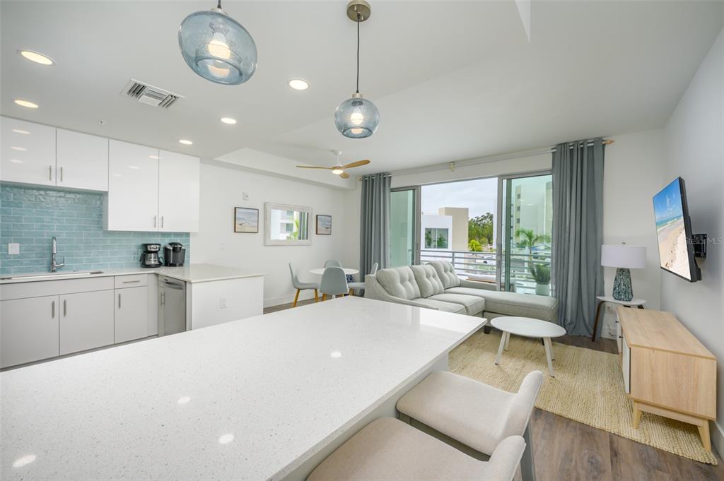 A modern open-concept kitchen and living area featuring white cabinetry, quartz countertops, and balcony access — 1703 N TAMIAMI TRAIL UNIT 207, SARASOTA, FL