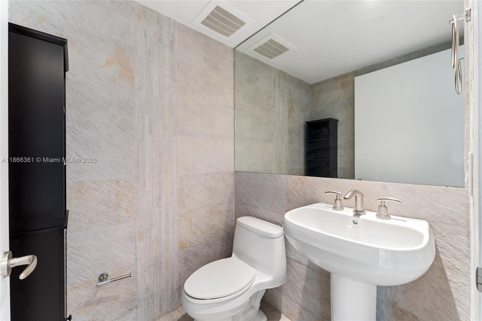 A bathroom features a pedestal sink, a toilet, and textured stone wall tiles — 901 Brickell Key Blvd # 2801, Miami FL 33131, MIAMI, FL