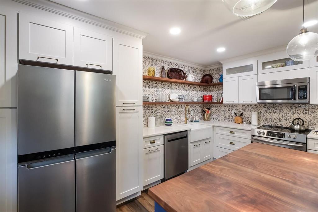 A kitchen features white cabinets, stainless steel appliances, open wood shelving, and patterned tile backsplash — 5400 34TH STREET W UNIT 15H, BRADENTON, FL