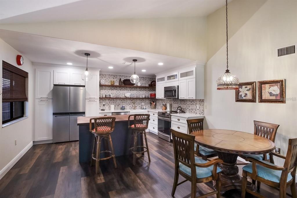 A kitchen with white cabinets, a dark island, open shelving, and a round dining table — 5400 34TH STREET W UNIT 15H, BRADENTON, FL