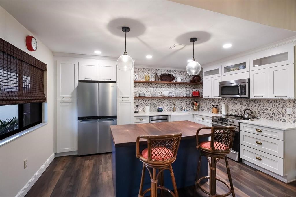 A kitchen features white cabinetry, a blue island with a wood top, and patterned backsplash tile — 5400 34TH STREET W UNIT 15H, BRADENTON, FL