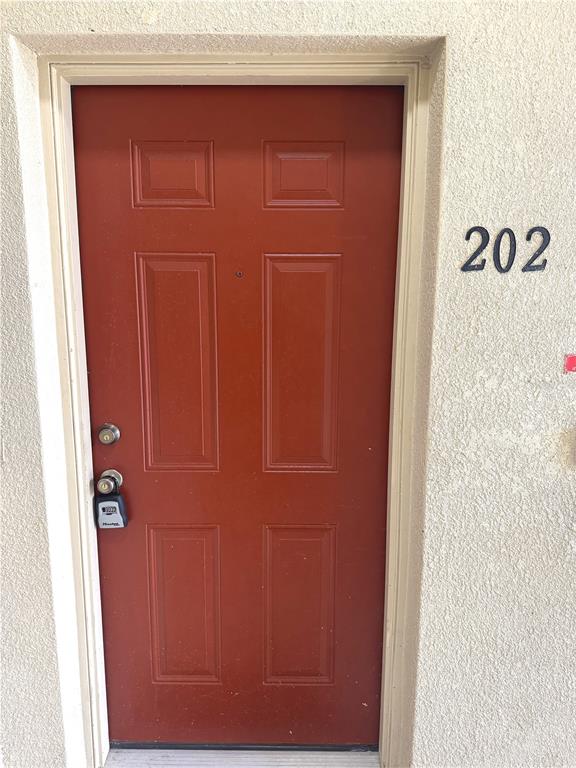 A red six-panel door with a lockbox is set into a textured beige exterior wall — 9621 LAKEDALE WAY UNIT 202, RIVERVIEW, FL