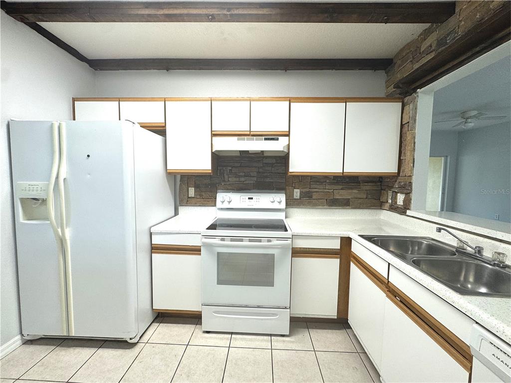 A kitchen features white cabinets, a white stove, a refrigerator, and a stone backsplash — 9621 LAKEDALE WAY UNIT 202, RIVERVIEW, FL