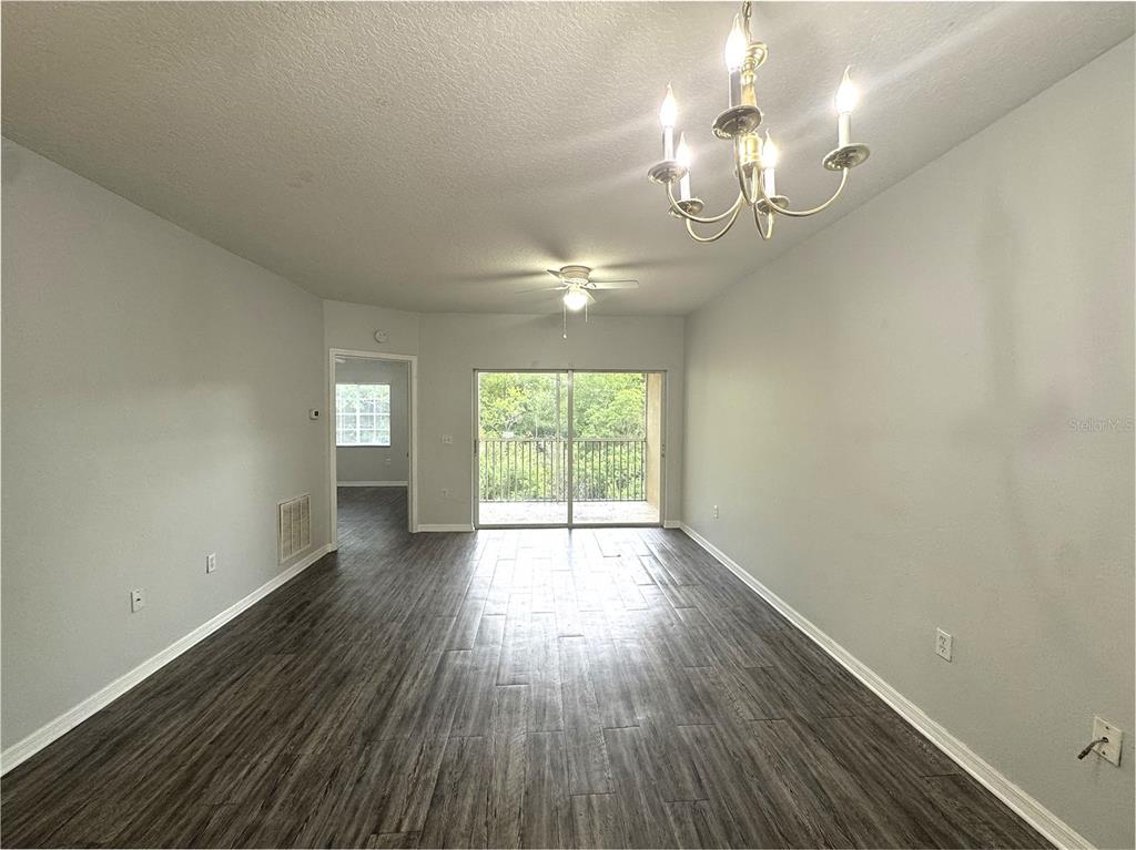 An empty living room features gray wood-look flooring, a chandelier, and a sliding glass door — 9621 LAKEDALE WAY UNIT 202, RIVERVIEW, FL