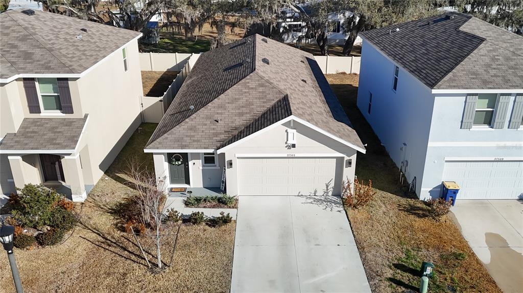 An aerial view shows a single-story house with a garage and a driveway between neighbors — 37501 SHARKS EYE LANE, ZEPHYRHILLS, FL