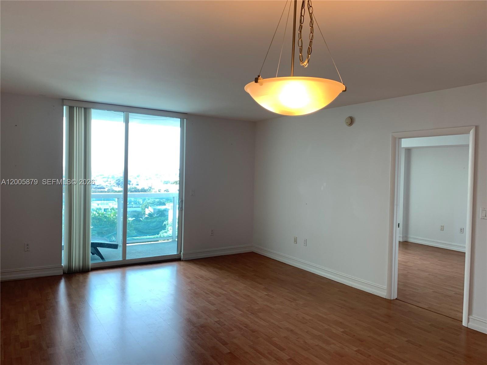 An empty room features wood-look flooring, a pendant light, and a sliding glass door balcony — 1800 N Bayshore Dr # 1506, Miami FL 33132, MIAMI, FL