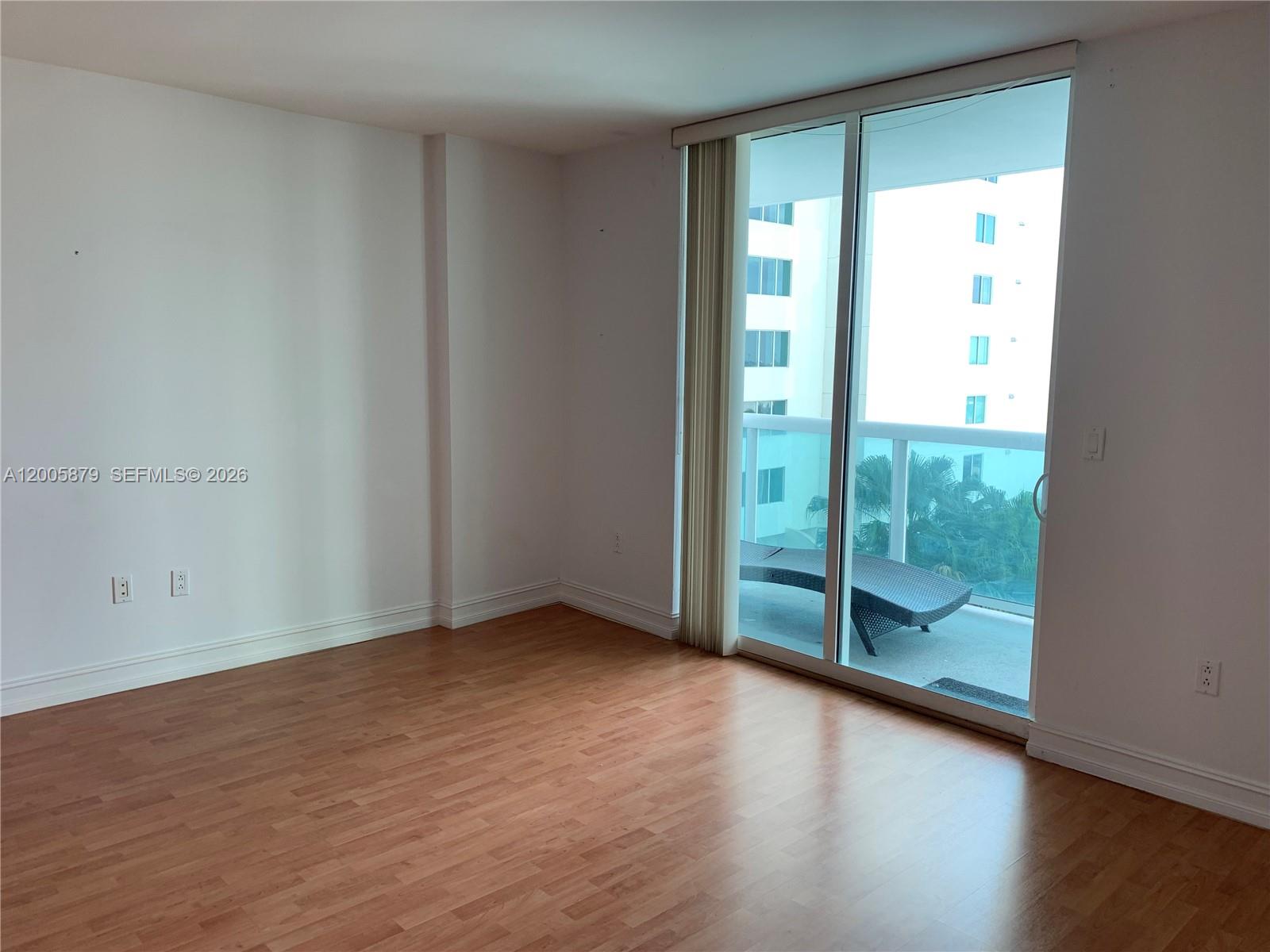 An empty room with wood-look flooring, white walls, and a sliding glass door to a balcony — 1800 N Bayshore Dr # 1506, Miami FL 33132, MIAMI, FL