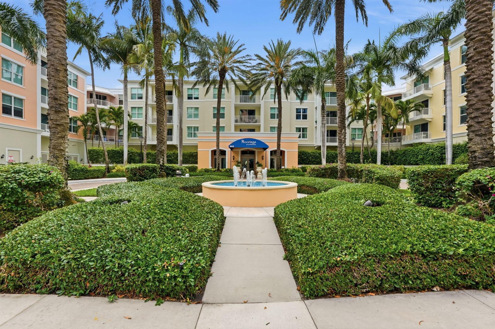 A multi-story apartment building features a central fountain, manicured hedges, and tall palm trees — 802 W Windward Way # 304, Lantana FL 33462, LANTANA, FL