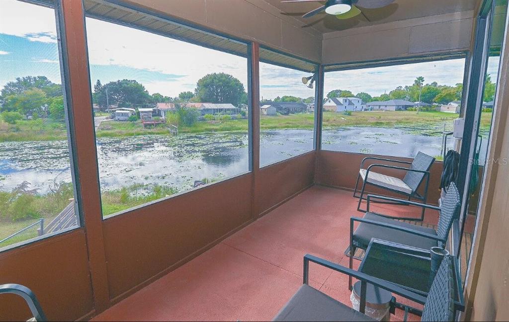 A screened-in porch features a red floor, outdoor furniture, and a view of a pond — 358 1ST AVENUE N, LAKE WALES, FL