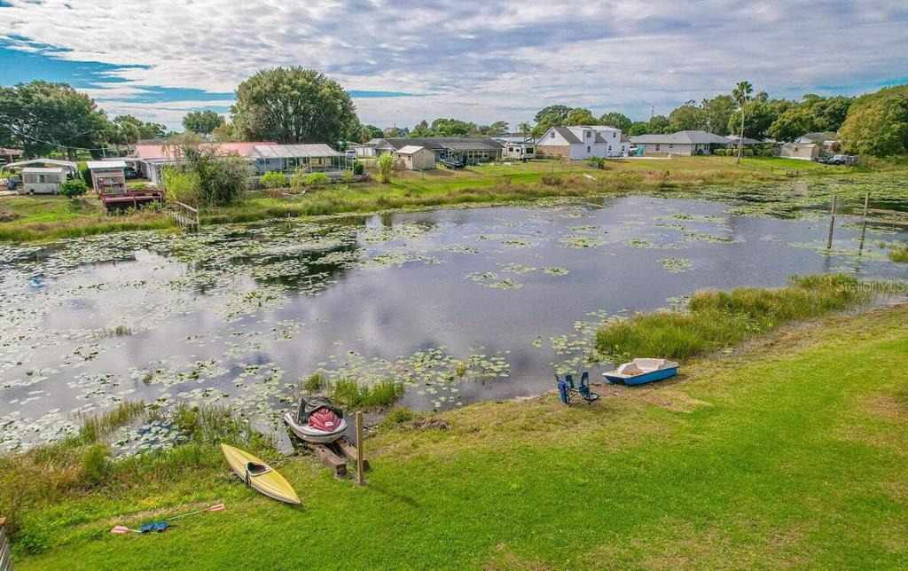 A grassy backyard slopes down to a pond with a kayak, jet ski, and boat — 358 1ST AVENUE N, LAKE WALES, FL