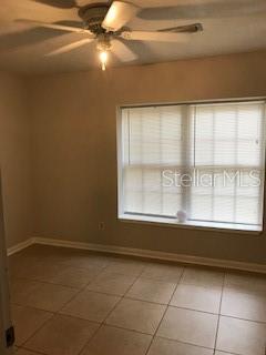 A bedroom with beige walls, tile flooring, a ceiling fan, and a large window with blinds — 1919 NANTICOKE CIRCLE, TALLAHASSEE, FL