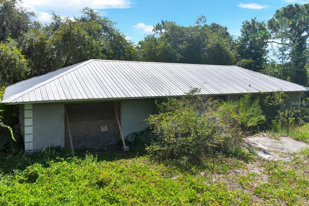 An exterior view of a single-story house with a metal roof and boarded-up windows — 2795 ABSHER ROAD, ST CLOUD, FL