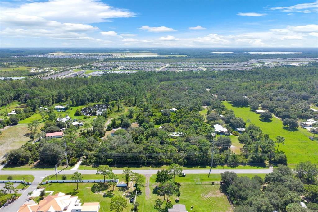 An aerial view shows a wooded residential area with scattered houses and a distant neighborhood — 2795 ABSHER ROAD, ST CLOUD, FL