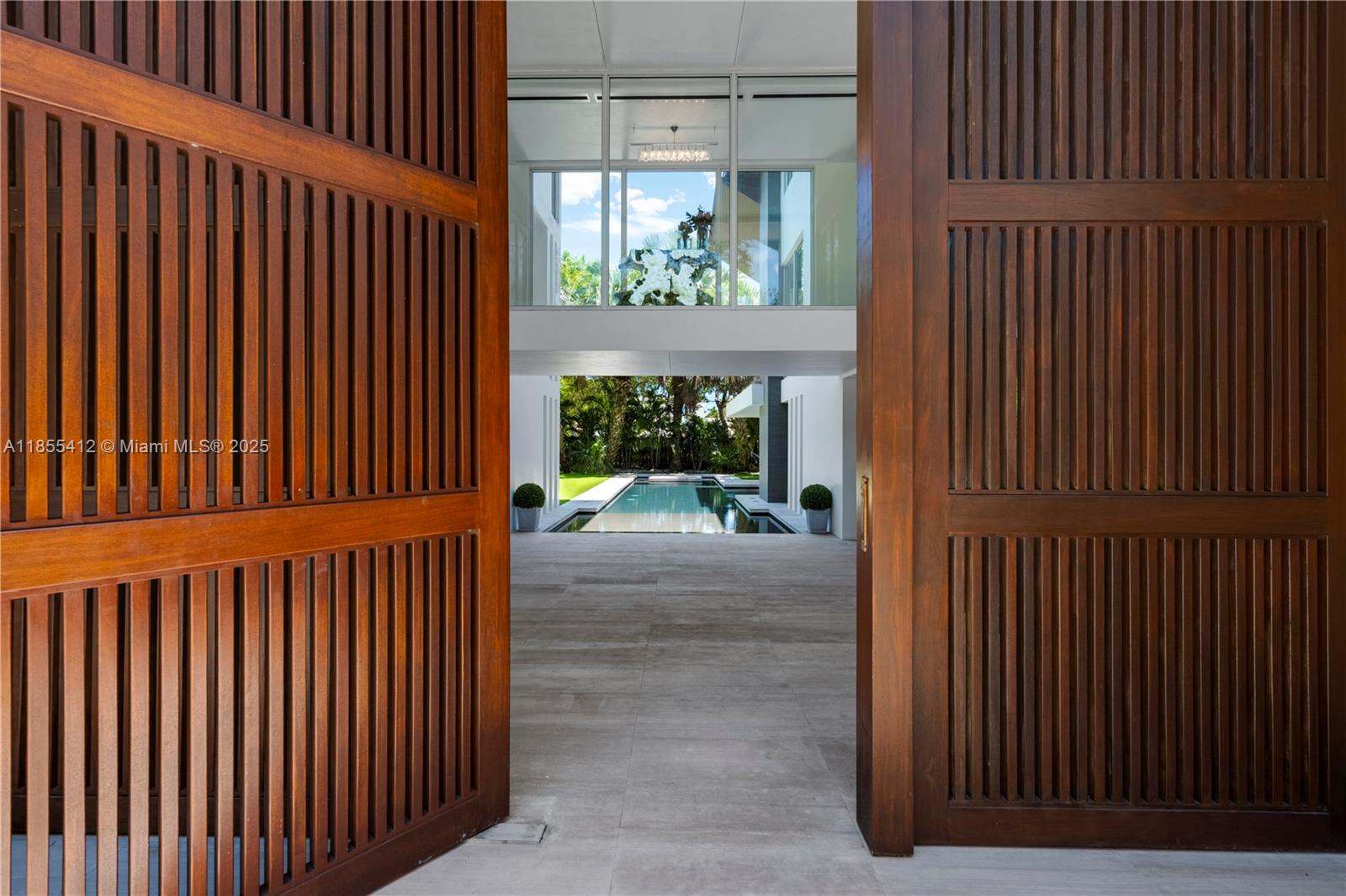 A view through large wooden slatted doors reveals a covered patio leading to a swimming pool — 545 SABAL PALM, Key Biscayne FL 33149, KEY BISCAYNE, FL