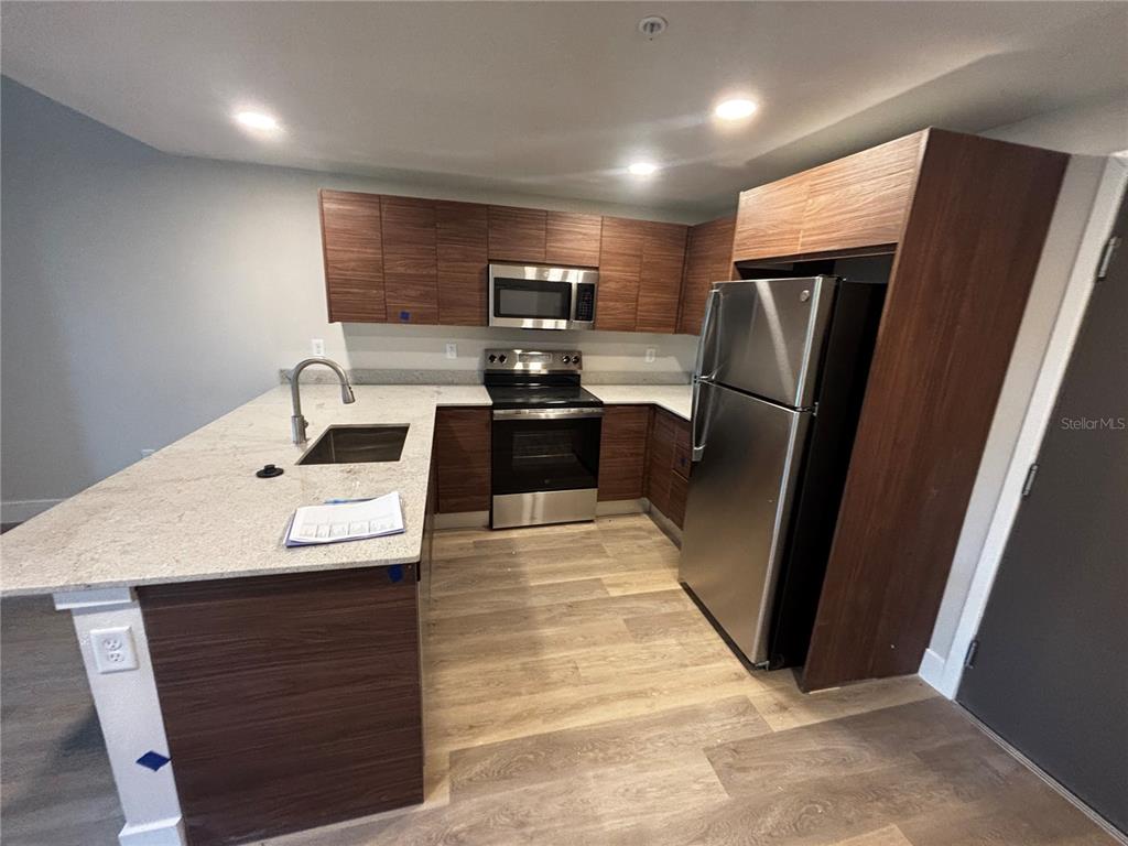 A kitchen features wood-grain cabinets, stainless steel appliances, and a light-colored granite countertop island — 4424 S TEXAS AVENUE UNIT 205, ORLANDO, FL