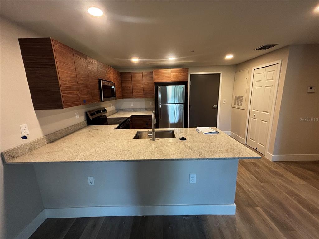 A kitchen features wood-grain cabinets, granite countertops, stainless steel appliances, and wood-look flooring — 4424 S TEXAS AVENUE UNIT 205, ORLANDO, FL