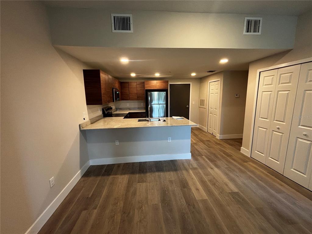 A kitchen with wood cabinets, granite countertops, and stainless steel appliances opens to a living area — 4424 S TEXAS AVENUE UNIT 205, ORLANDO, FL