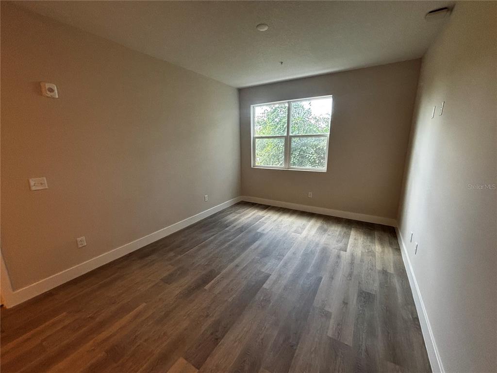 An empty bedroom features light-colored walls, wood-look flooring, and a window overlooking trees — 4424 S TEXAS AVENUE UNIT 205, ORLANDO, FL