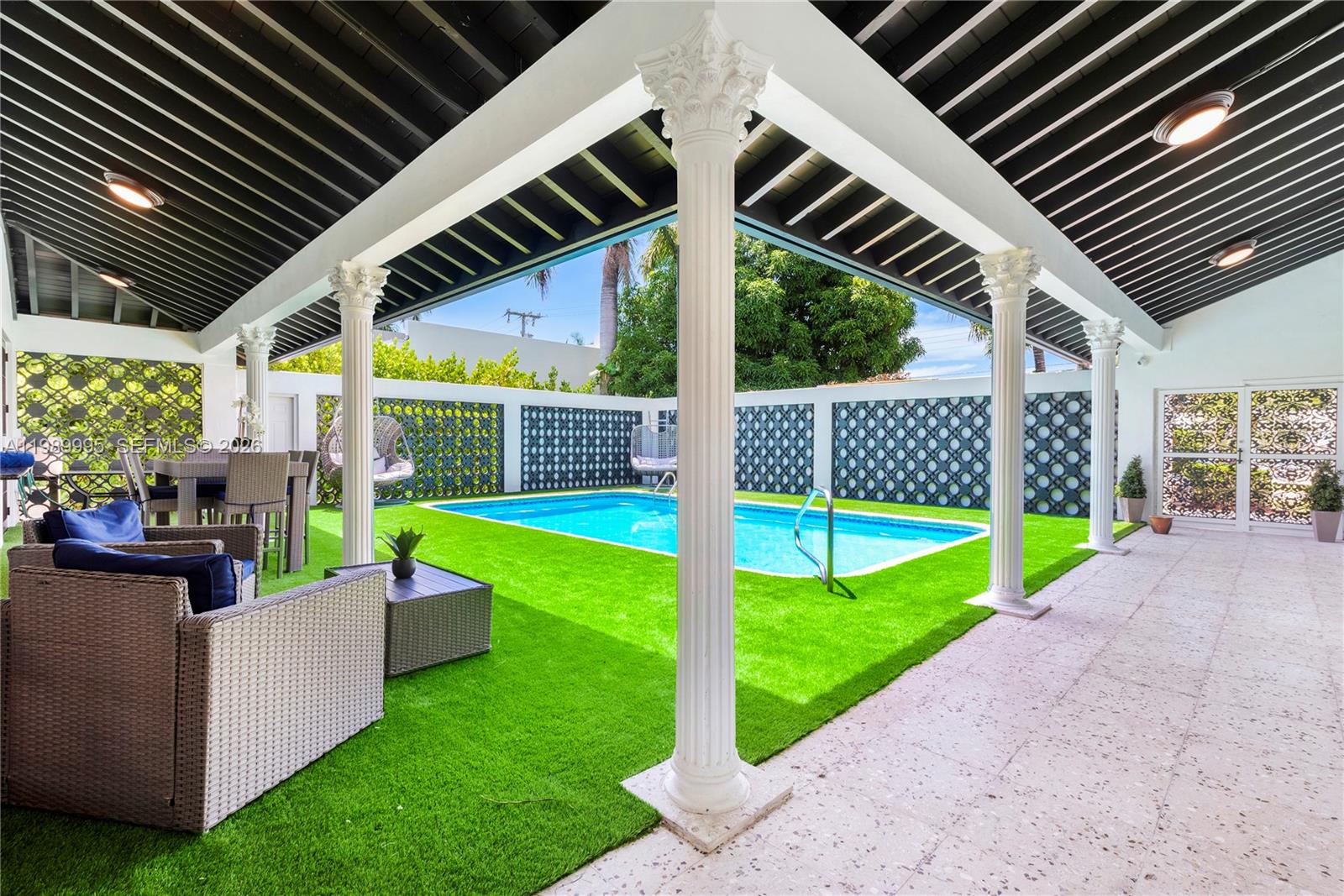 A covered patio with white columns overlooks a rectangular swimming pool and artificial grass lawn — 472 Sunset Dr, Hallandale Beach FL 33009, HALLANDALE BEACH, FL