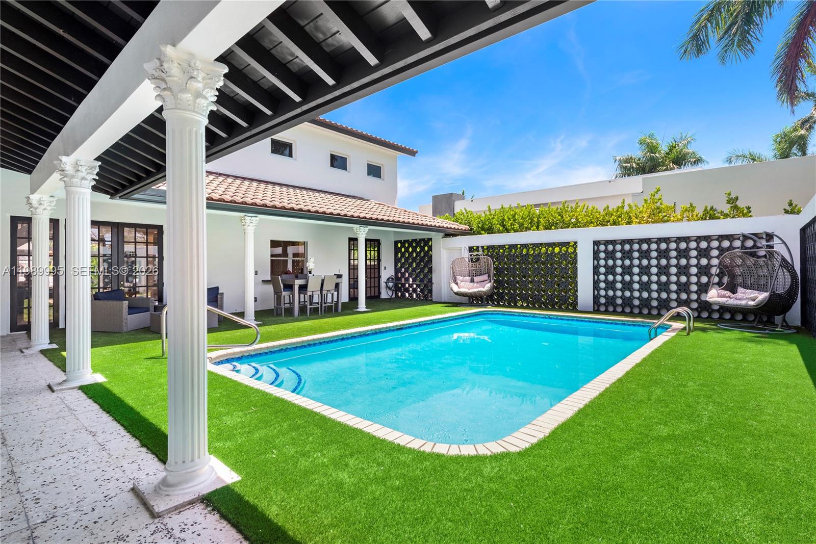 A swimming pool with artificial turf sits in a courtyard featuring white columns and walls — 472 Sunset Dr, Hallandale Beach FL 33009, HALLANDALE BEACH, FL
