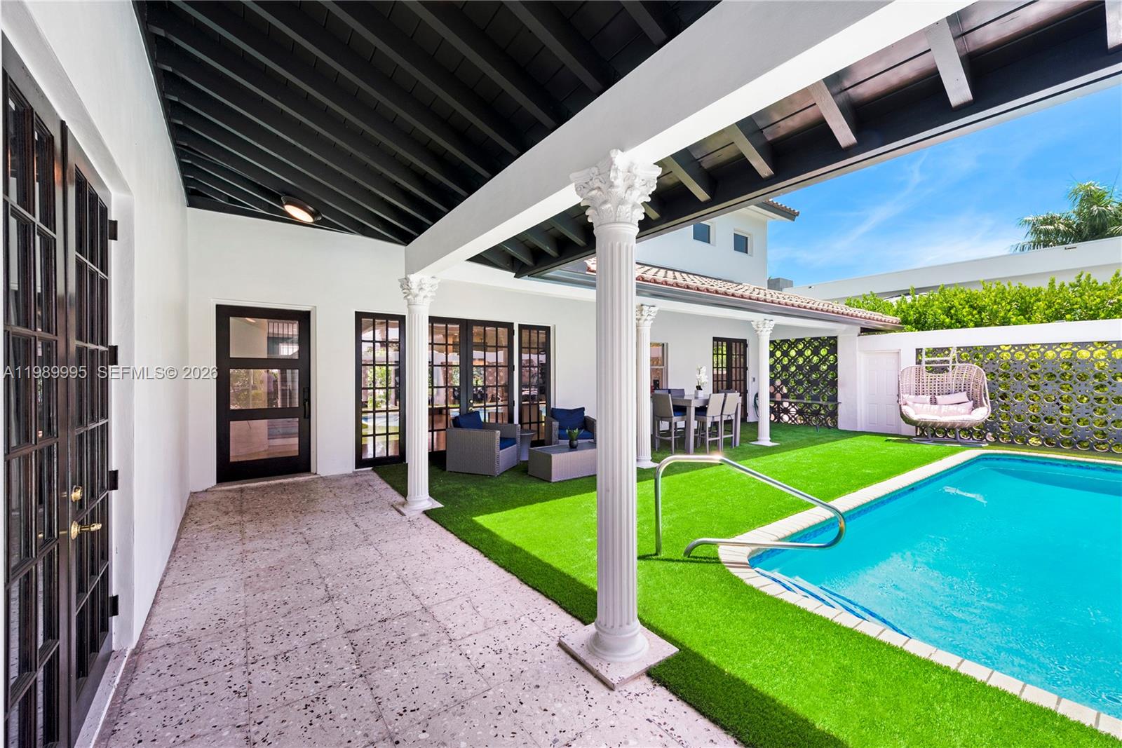 A covered patio with a pool, artificial turf, and white columns overlooks a backyard — 472 Sunset Dr, Hallandale Beach FL 33009, HALLANDALE BEACH, FL