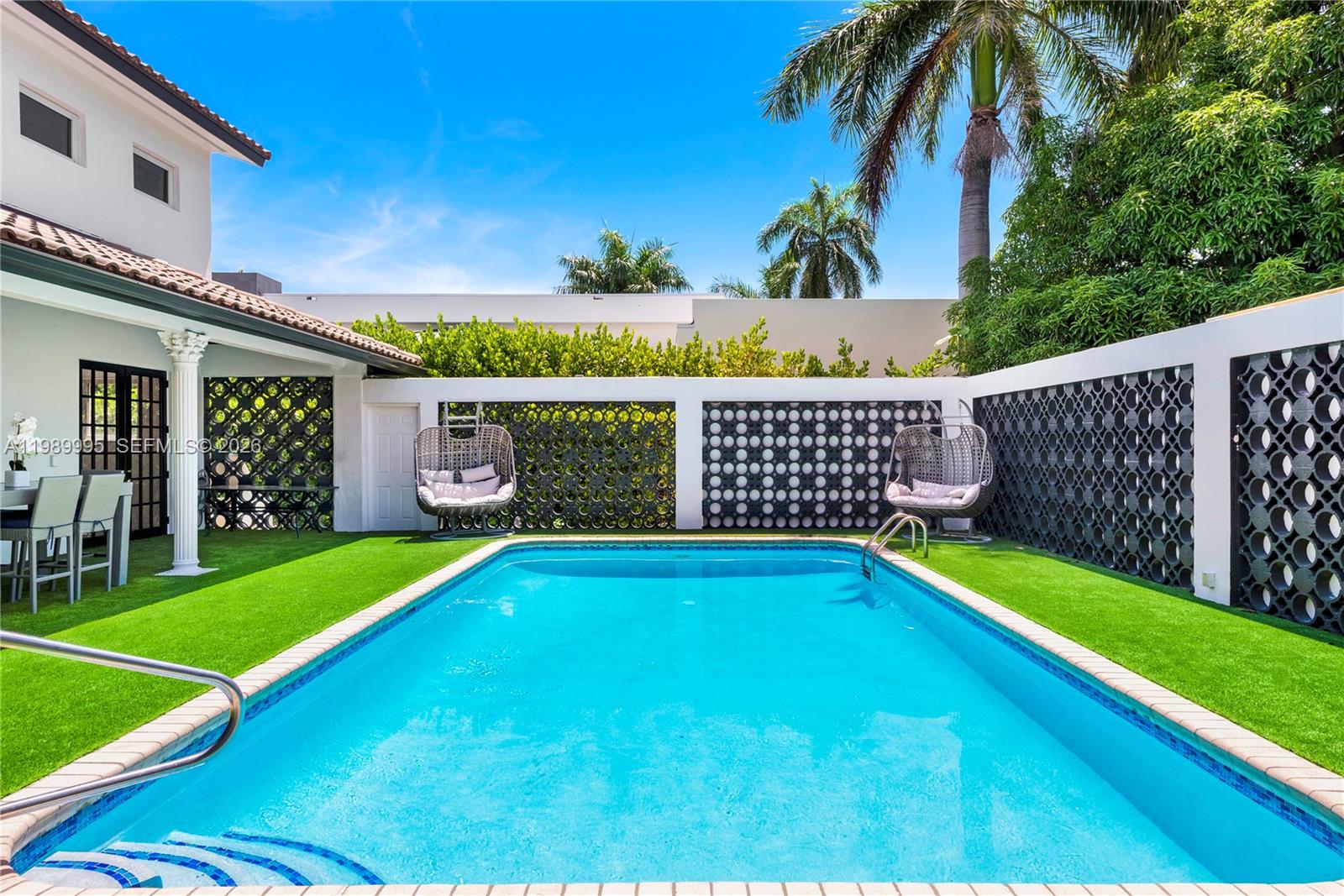 A rectangular swimming pool sits in a backyard with artificial turf and decorative privacy screens — 472 Sunset Dr, Hallandale Beach FL 33009, HALLANDALE BEACH, FL