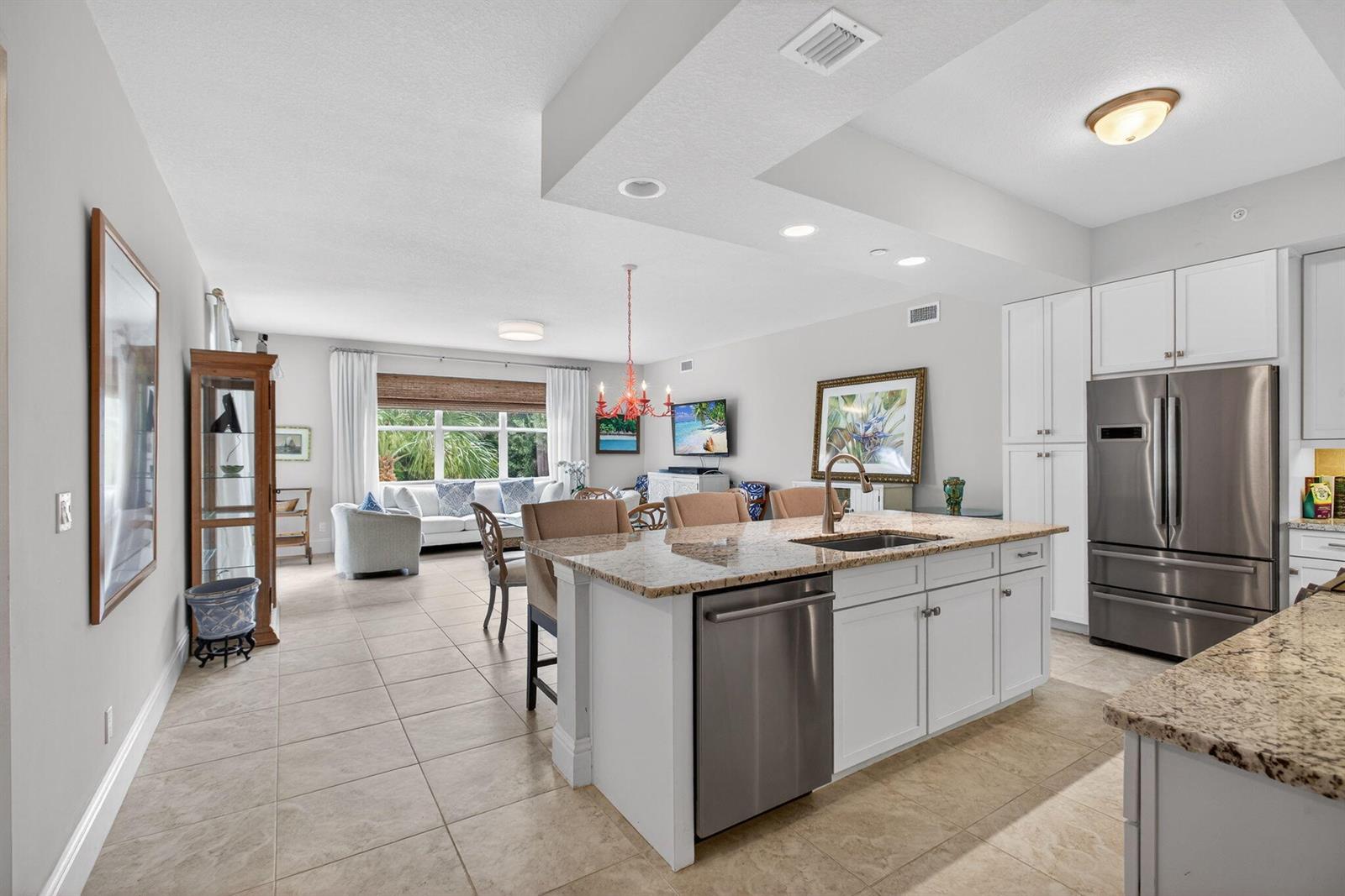 An open-concept kitchen with a granite island overlooks a living and dining area — 834 Bay Colony Drive S, Juno Beach FL 33408, JUNO BEACH, FL
